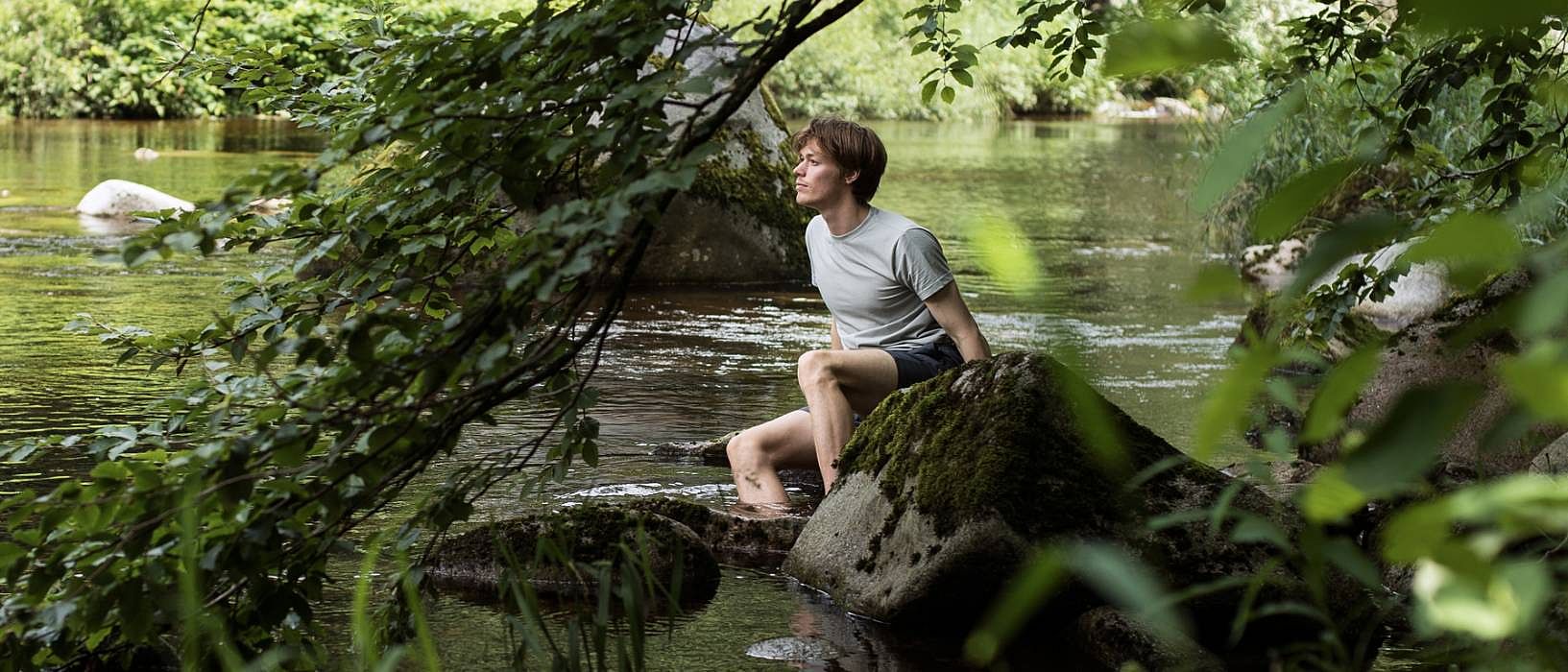 Man sitter på en sten vid en å