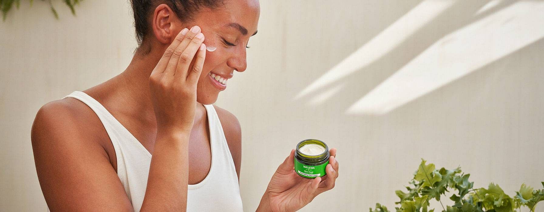 Kvinna smörjer in ansiktet med Weleda Skin Food