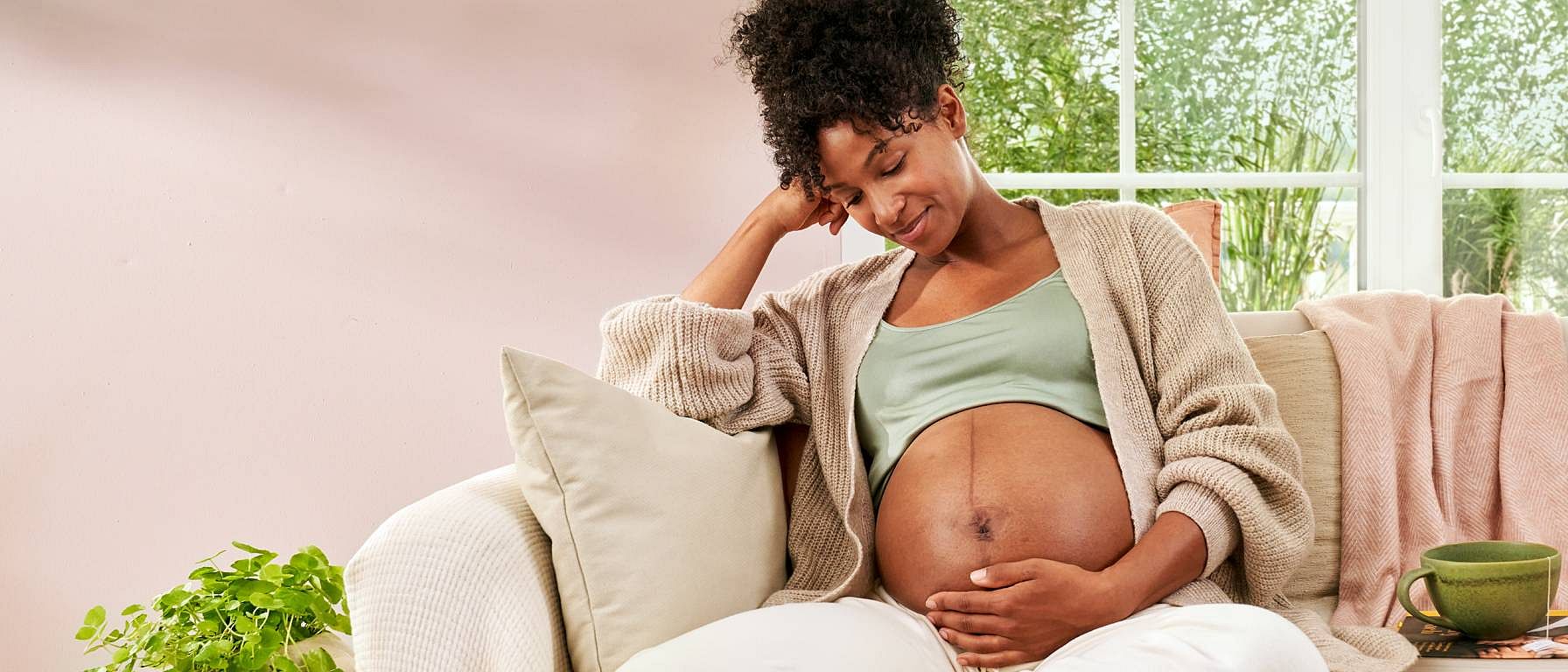 Gravid kvinna sitter i soffan men handen på magen.
