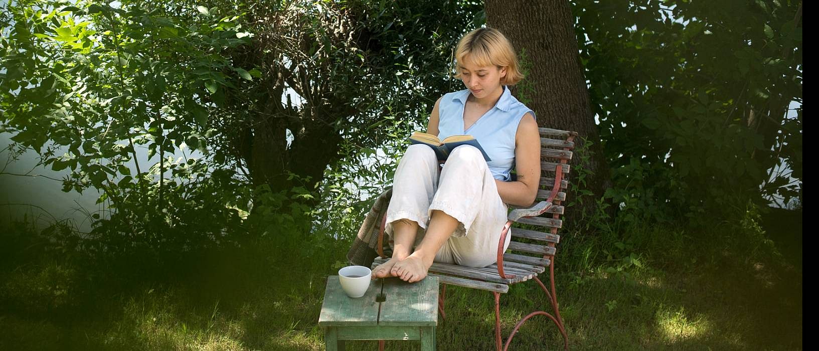 kvinna sitter på en stol vid vattnen och läser en bok
