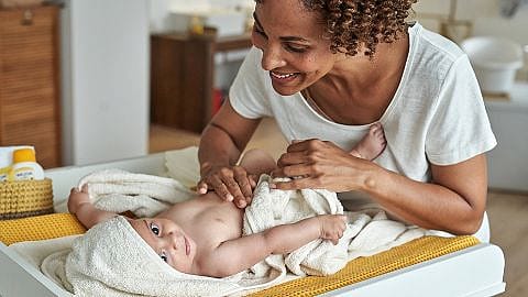 Glad mamma med bebis på ett skötbord