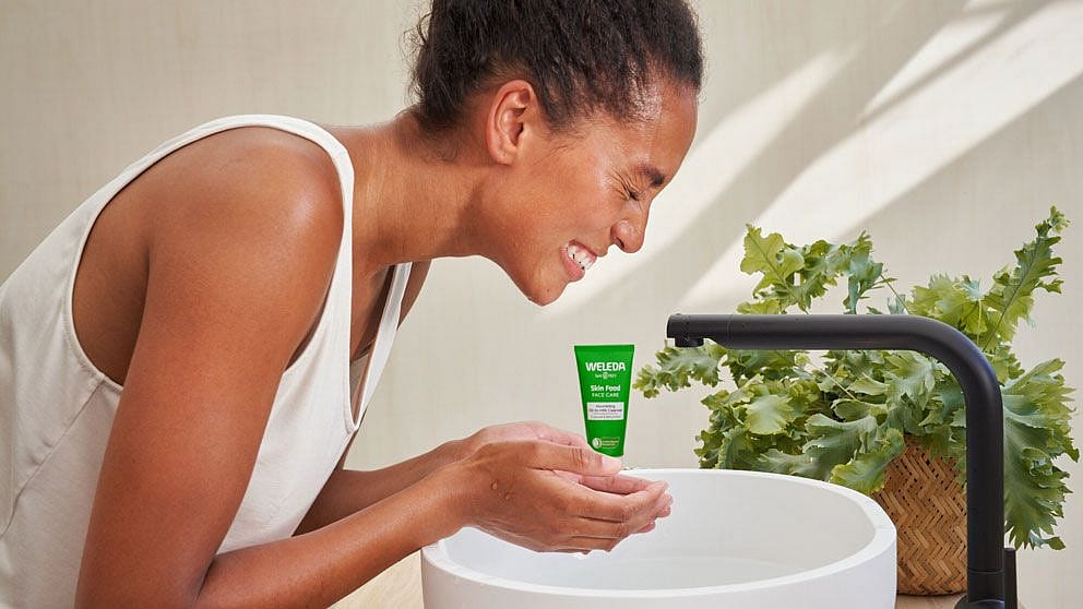 Kvinna tvättar ansiktet med Weleda Skin Food Nourishing Cleansing Balm!
